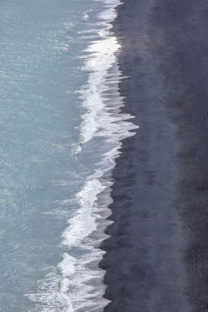 Waves of the Atlantic ocean fall on the black sand of the beach of Iceland from a height