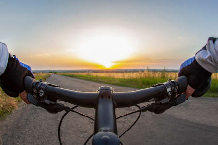 cyclist in gloves rides along the road towards the sunny sunset sky. Sports and travel.の写真素材
