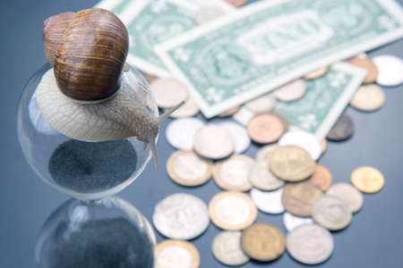 snail crawls on an hourglass against the background of money. speed and stability in increasing income. time for work and rest. financial business success. time investment targetの写真素材
