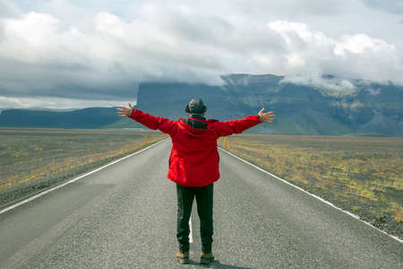 Tourist stands on the road against the mountain landscape in Iceland