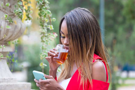 Beautiful young African girl with a Cup of tea and a phone in her hands in the Park