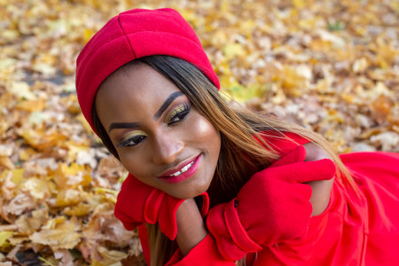 Beautiful African girl in red clothes resting in autumn leavesの写真素材