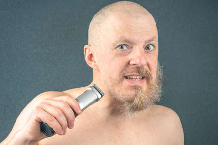 Bearded man with trimmer to adjust beard in hand. grooming and fashionable style barbershop. Beard...