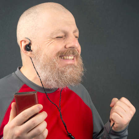 bearded man likes to listen to his favorite music at home with an audio player in small headphones....