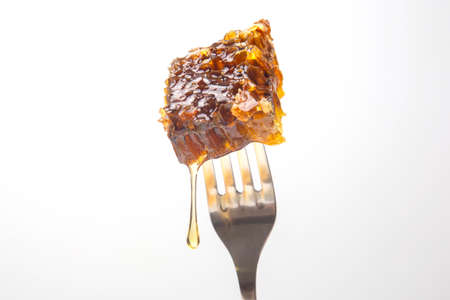 Drops of fresh honey drip from wax honey on a table fork. vitamin nutrition and bee product.の写真素材
