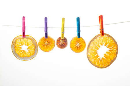 dried pieces of different citrus fruits hang on colored clothespins on white background