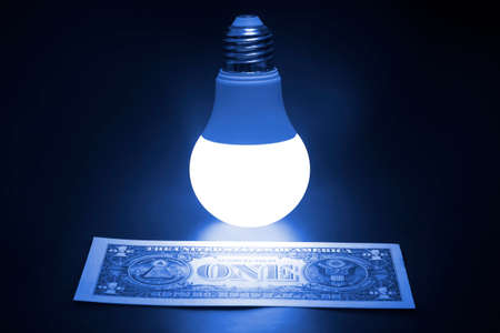 Glowing LED lamp and one dollar bill on a dark background. Business and savings. Modern technology and electricityの写真素材