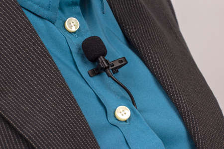 The lavalier microphone is secured with a clip on a blue women's shirt close-up. Audio recording of the sound of the voice on a condenser microphone.の写真素材