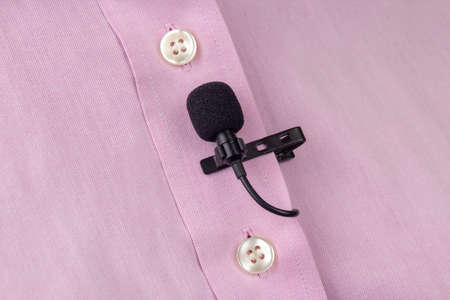 A clip-on lavalier microphone is attached to a pink shirt, close-up. Audio recording of the sound of the voice on a condenser microphone.の写真素材