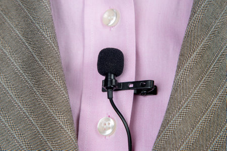 The lavalier microphone is secured with a clip on a women's shirt close-up. Audio recording of the sound of the voice on a condenser microphone.の写真素材