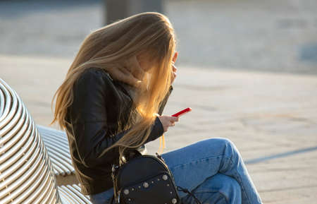 Woman with mobile phone sitting on a benchの写真素材
