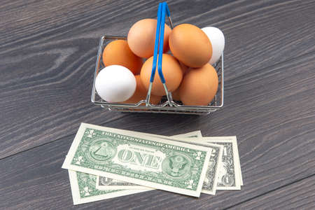 chicken eggs in a supermarket grocery basket against a dollar background on a wooden background....