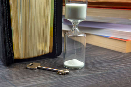 key next to the hourglass on the background of books. metaphor for discovering wisdom through the...