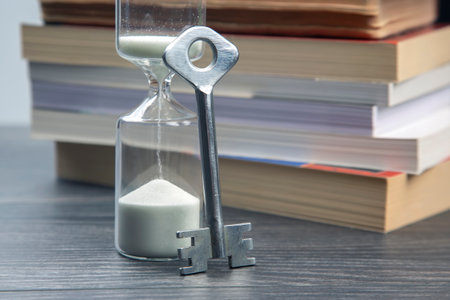 key next to the hourglass on the background of books. metaphor for discovering wisdom through the...