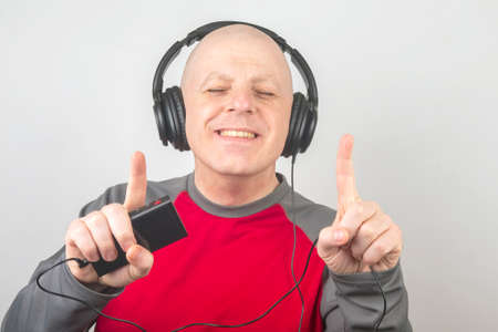 man with closed eyes listens to music with headphones on a light backgroundの写真素材