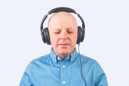 portrait of a man in a blue shirt with headphones in relaxation listening to music on a light...