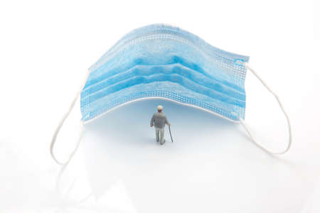 miniature people. a figurine of an elderly man protected from illness next to a medical mask. the...