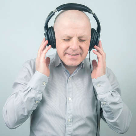 man with closed eyes listens to music with headphones on a light background