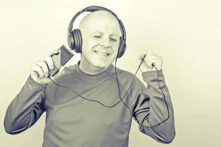 smiling man with headphones and digital portable player in hand relaxes while listening to