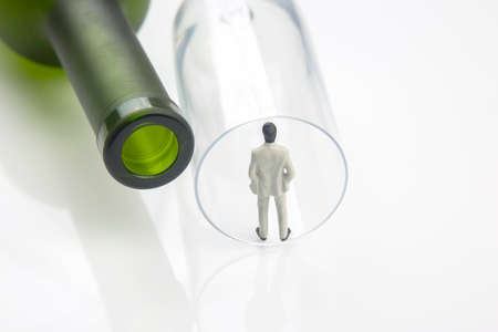 miniature people. alcohol addiction problem concept. an alcoholic stands on the edge of a glass near a wine bottleの写真素材