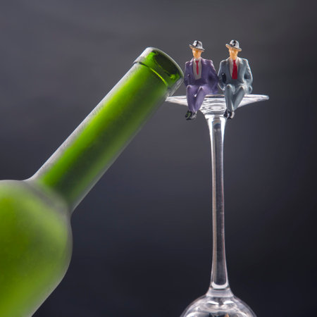 miniature people. alcohol addiction problem concept. two man sit on the edge of a wine glass near the bottleの写真素材