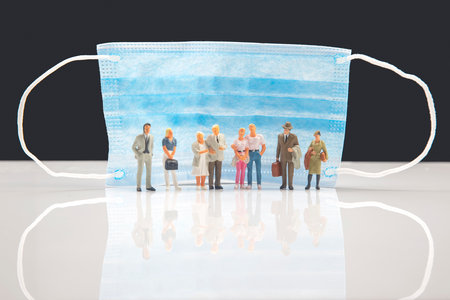 miniature people. figurines of family people protected from illness next to a medical mask. the concept of protection from a viral pandemic in societyの写真素材