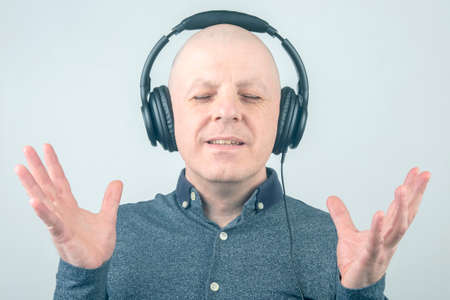 man with closed eyes listens to music with headphones on a light background