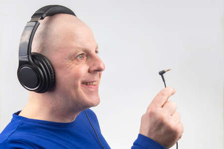 bald man with headphones on his head and an open plug in his hand. Search for a sound source