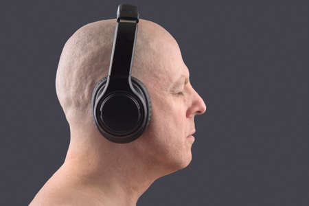 man with closed eyes listens to music with headphones on dark backgroundの写真素材