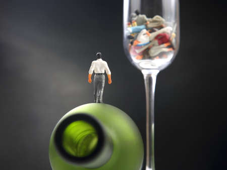 miniature people. man addicted to alcohol is walking on a bottle against the background of a glass with ruined lives. the problem of alcoholism in societyの写真素材