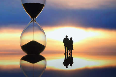 miniature people. silhouettes of people watching the sunset on the background of the hourglass. end of life.の写真素材