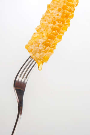 Drops of fresh honey drip from wax honey on a table fork. vitamin nutrition and bee productの写真素材