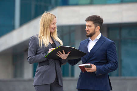 successful businessmen partners man and woman on the background of a business building with documents in their hands discussing business projectsの写真素材
