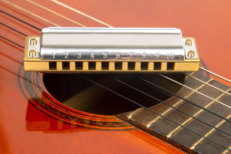 The harmonica rests on the body of a classical guitar. Classical musical wind instrument.