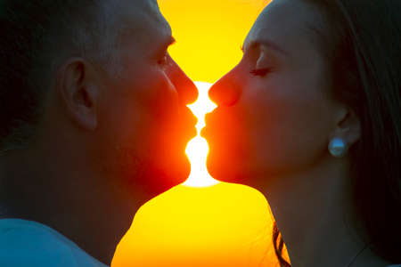 silhouette in profile of the faces of a man and a woman against the backdrop of the setting sun....