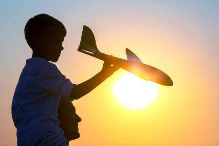 Silhouette of a boy launches a model airplane into the sky against the backdrop of the setting sun. The childhood dream of the future pilotの写真素材