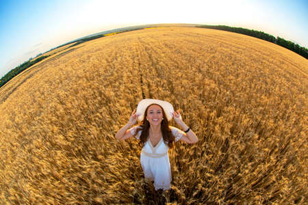 Happy woman stands in a wheat field in the summer against the background of a setting sunの写真素材