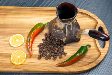 fresh coffee beans fall out of broken ceramic coffee brewing utensils on wooden board next to pepper and lemonの写真素材