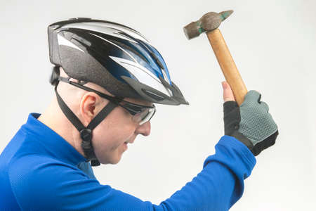 male cyclist in sports glasses and a bicycle helmet with a hammer in his hands demonstrates the protection of his head from injury. sports protection concept for active sportsの写真素材