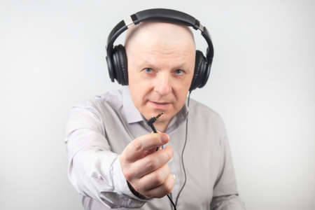 bald man with headphones on his head and an open plug in his hand. Search for a sound sourceの写真素材