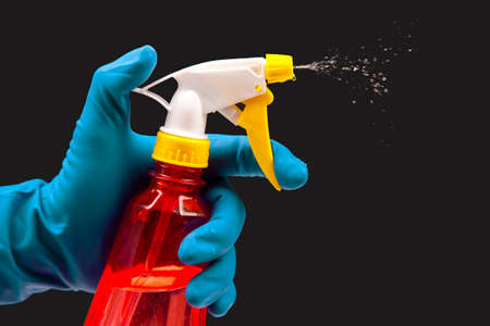 water sprayer bottle in a hand with gloves on a dark background with liquid spray. household items...