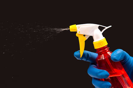 water sprayer bottle in a hand with gloves on a dark background with liquid spray. household items for homeの写真素材