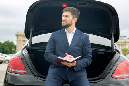Successful businessman sits with a diary on the hood of his prestigious carの写真素材