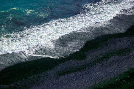 Waves of the Atlantic ocean fall on the black sand of the beach of Iceland from a height