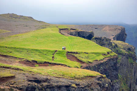 Two people are walking along the mountain green slope of Iceland. Travel and tourismの写真素材