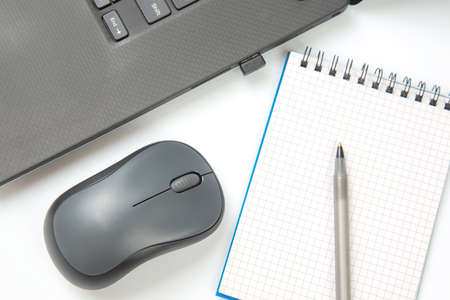 Computer wireless mouse, pen and notepad next to a laptop on a white table close-up. Items for office workの写真素材