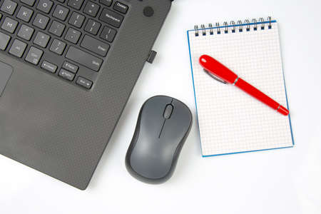 Computer wireless mouse, pen and notepad next to a laptop on a white table close-up. Items for office workの写真素材