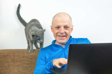 man with a gray cat looks at a laptop screen. freelancer business works at home. relationship with a catの写真素材