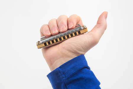 The right hand holds a harmonica on a white background. Classical musical wind instrument.の写真素材