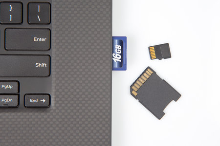 sd memory card for recording electronic data near a laptop on a white background. electronic...